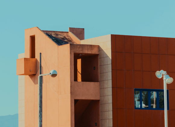 Modern building exterior with geometric shapes, earth-toned colours, and two street lamps in the foreground.
