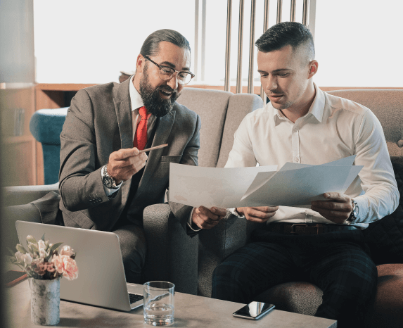 Two men in suits reviewing paperwork together, one pointing to a document.