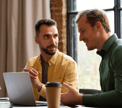 Two men looking at a laptop together, engaged in a conversation.